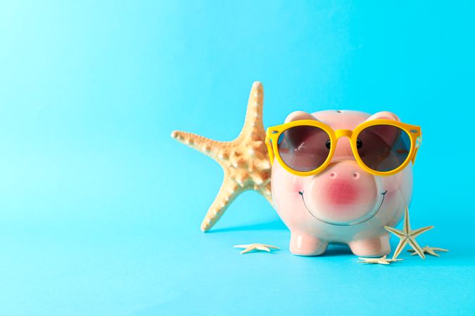 Happy piggy bank with sunglasses and starfishes on color background, space for text. Finance, saving money