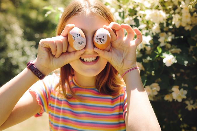 Portrait of a smiling girl holding two painted easter eggs to her eyes