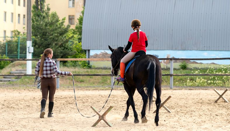 Instructor leading young rider during training session outdoors.