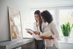 Two cheerful multi-ethnic creative businesswomen with tablet working on