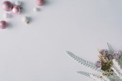 Pink baubles and flowers with snowy leaves in corners of light background