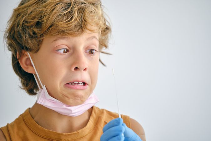 Scared boy with crop nurse during COVID test in clinic