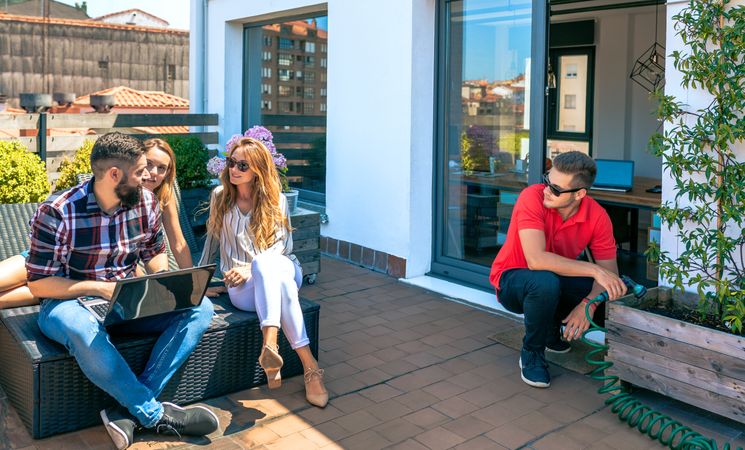 Colleagues talking in a coffee break while man watering plants in office rooftop