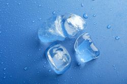 Looking down at top view of four melting ice cubed on blue table