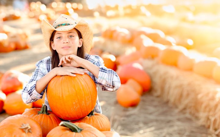 Girl Wearing Cowboy Hat Enjoying The Pumpkin Patch on a Sunny Fall Day.