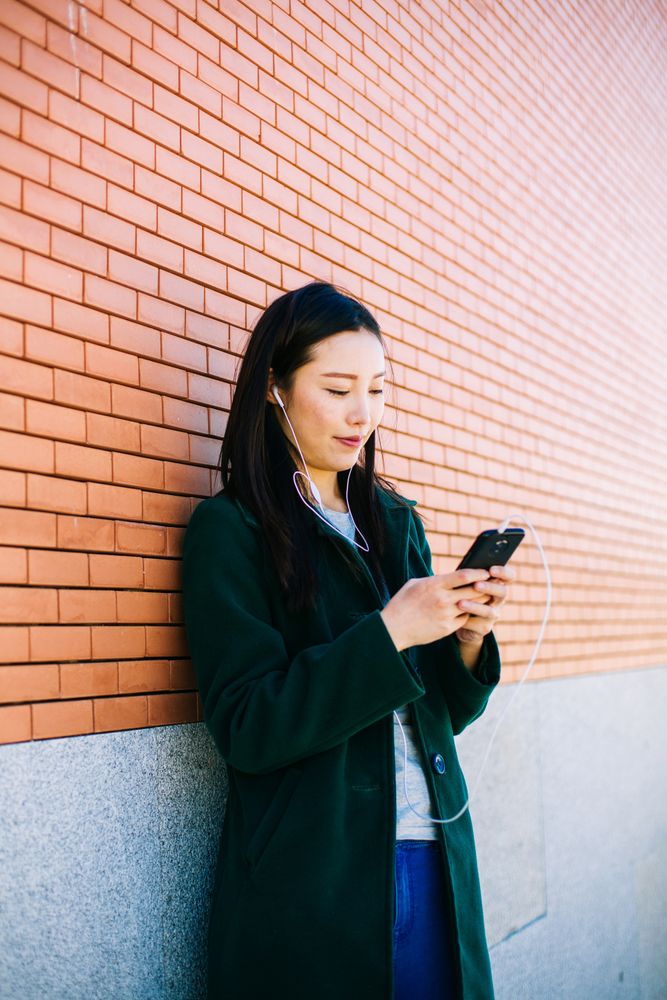 Asian female listening to music near brick wall
