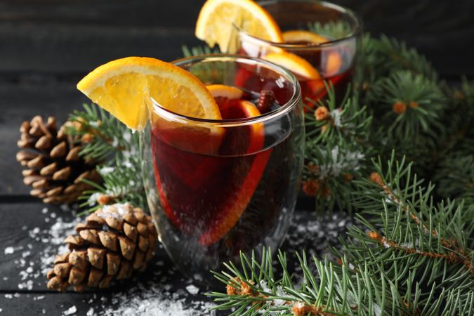 Glasses of tasty mulled wine with orange on decorated wooden background, close up
