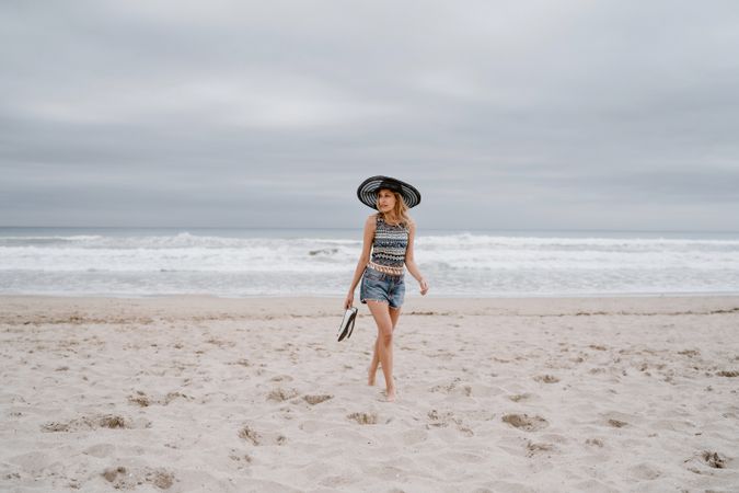 Young female walking barefoot on sandy beach