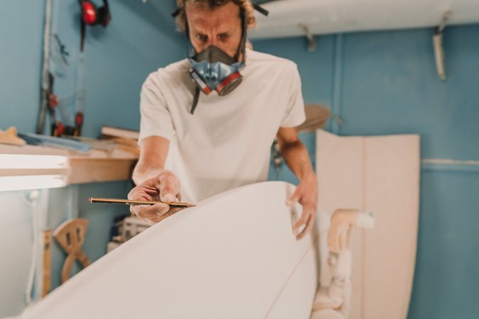 Man in respirator measuring surf board in workshop