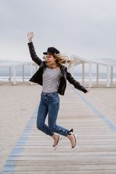 Joyful woman jumping raising hands up on wooden beach pier