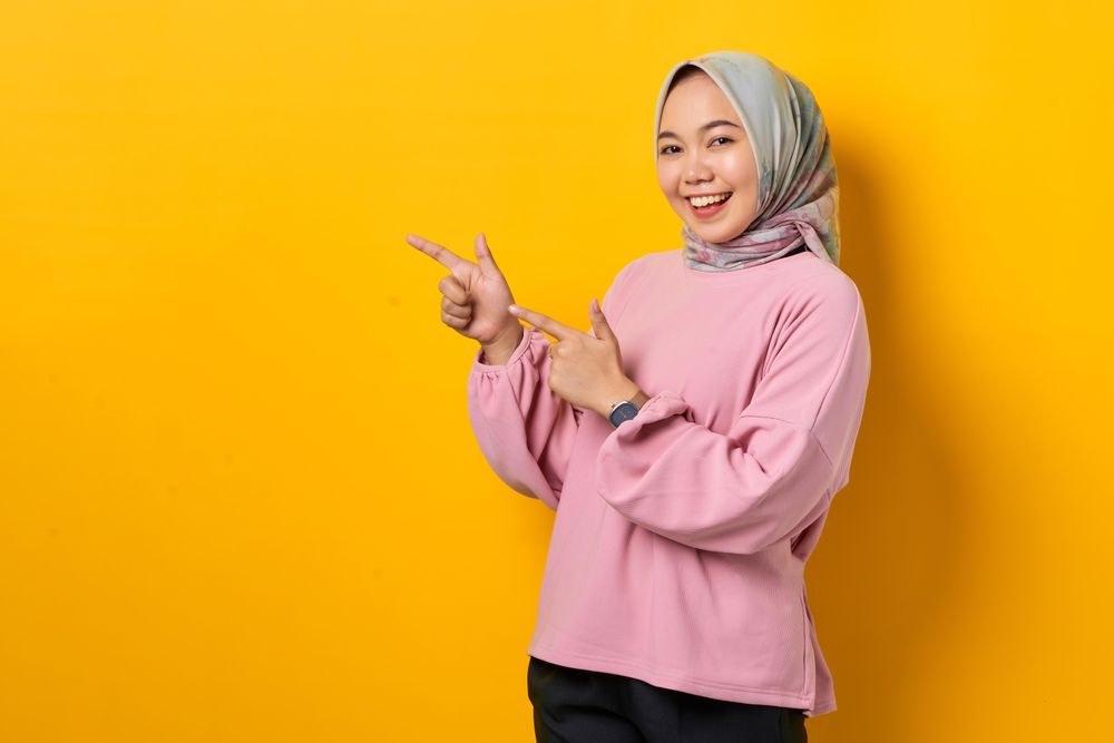 Happy Muslim woman in headscarf pointing to space beside her