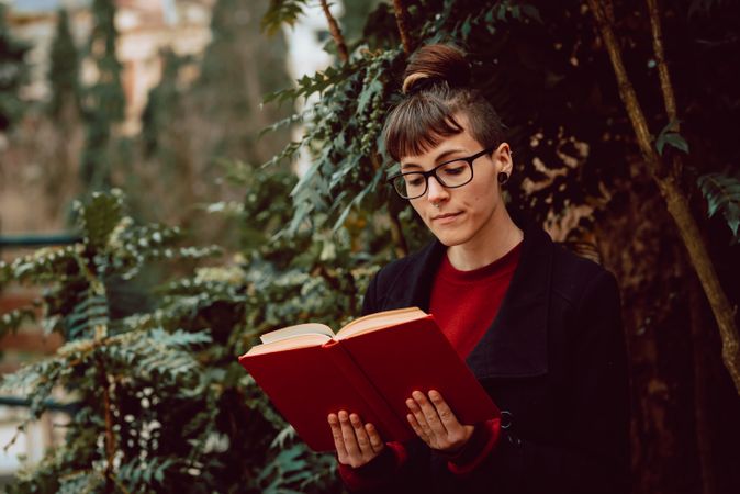 Young woman reading book on bench in park