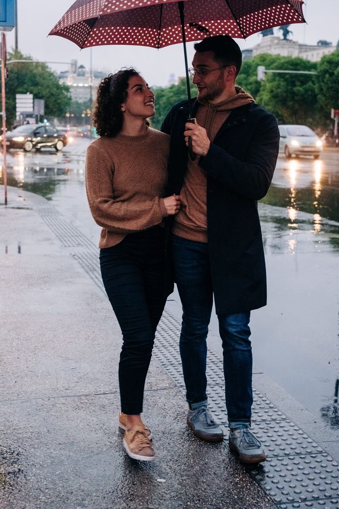 Happy couple with umbrella hugging on wet street