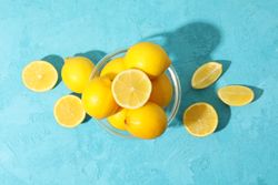Bowl with lemons on blue background, top view. Ripe fruit