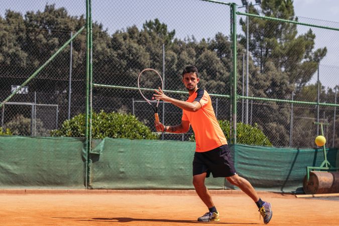 Man in sportswear playing tennis on a dirt tennis court