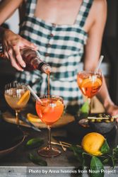 Young woman in checkered dress pouring aperitif with orange slices 49NP6b
