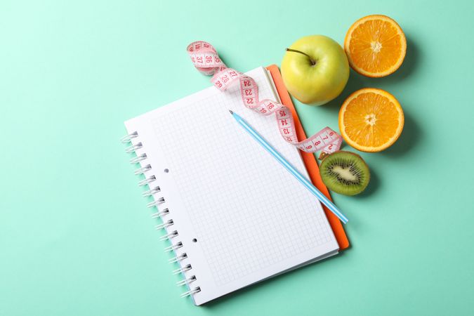 Notebook, measuring tape, pen and vegetarian food on mint background. Weight loss