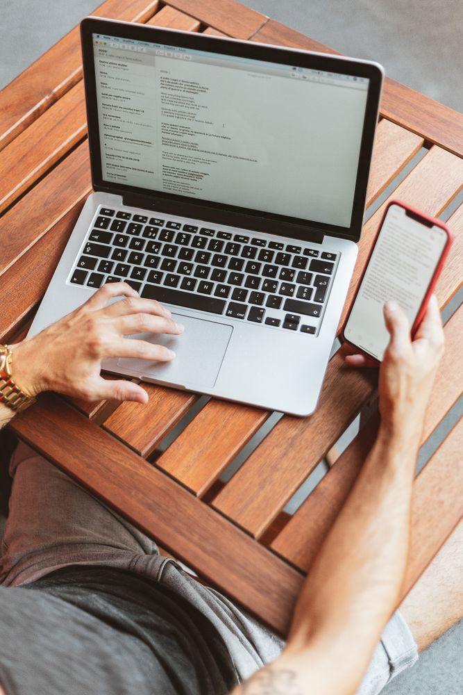Cropped image of a man using laptop and computer on wooden table