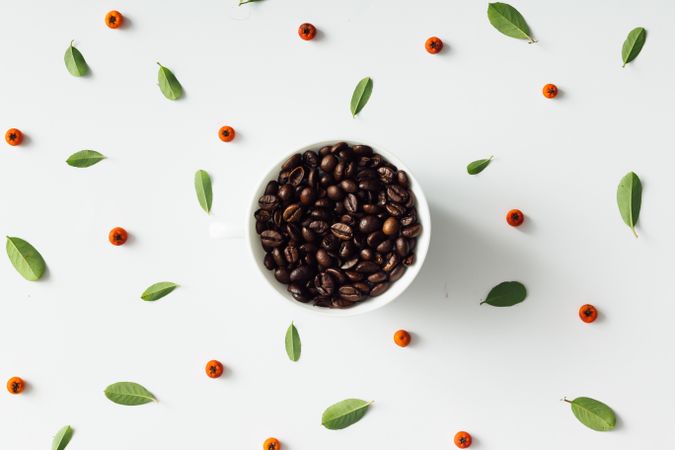 Coffee cup filled with coffee beans on pattern of coffee fruit and leaves on light background