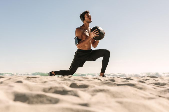 Young man lunging with weighted ball on seashore