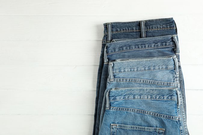 Different jeans folded on a wooden background, space for text