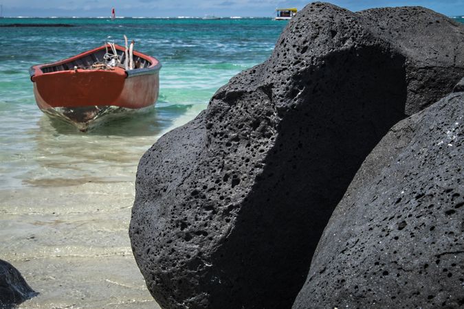 Small red boat next to dark lava rock in tropical waters