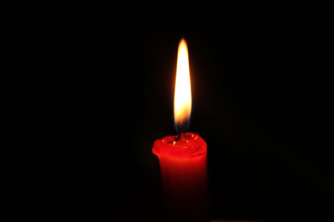 Red candle burning brightly on dark background