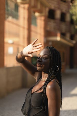 Close-up portrait of a young Black woman blocking sunlight from her face with her hand in the street