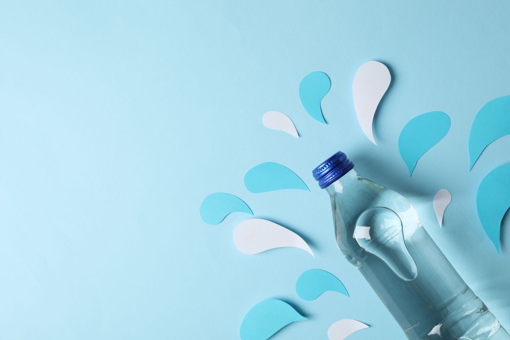 Looking down at full water bottle with decorative cut out water pieces, copy space