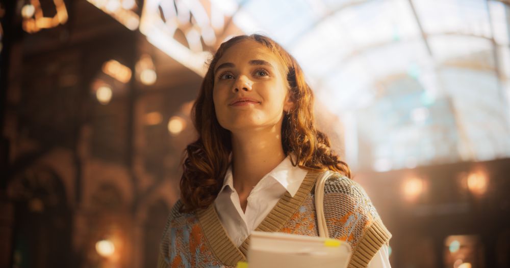 Confident Young Female Student Carrying Books in a Grand Library.