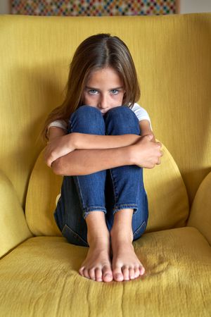 Sad girl sitting in armchair at home