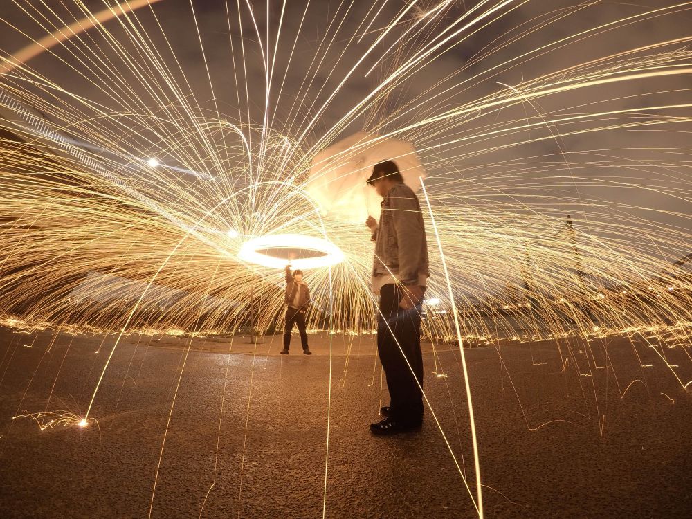 Long shot of a person making circular motion with light while another person holding an umbrella