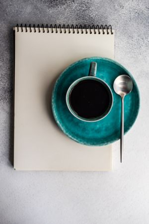 Top view of coffee cup on teal plate and notepad