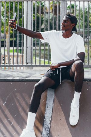 Sportive black men taking selfie with smartphone while sitting on fence