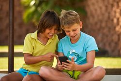 Cheerful boys browsing smartphone on sunbed