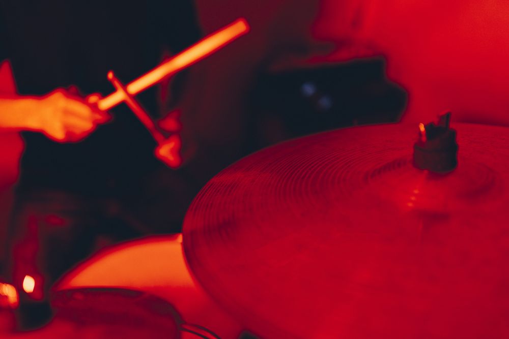 Anonymous man with drumsticks playing on drums in redness