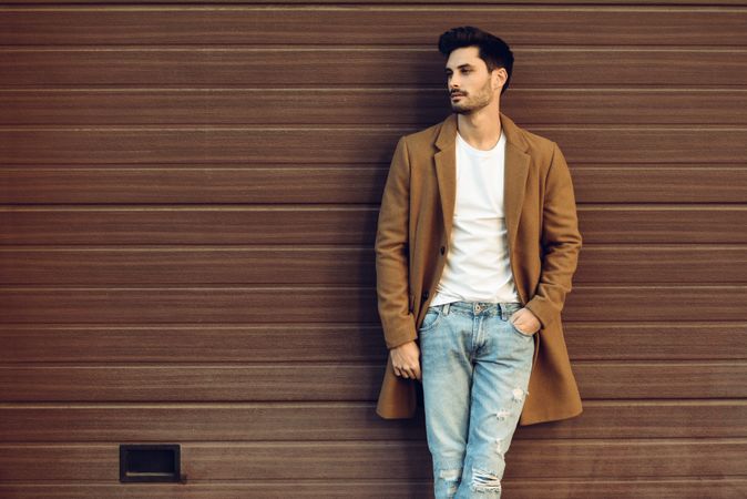 Man leaning on brown wall in winter coat looking to his side
