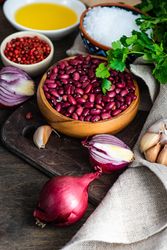 Bowl of dried kidney beans surrounded by onions, garlic, peppercorn, salt, oil and parsley