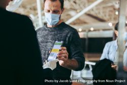 Man in face mask showing his covid-19 vaccine passport on cell phone to airport staff 0vaDgb