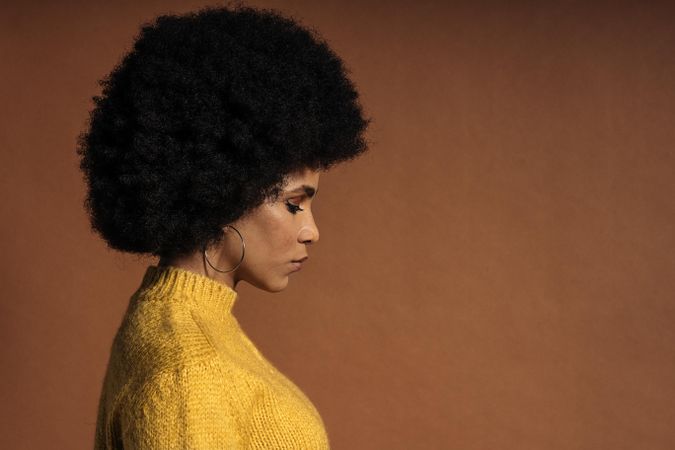 Side view of sad woman yellow knit sweater against brown background