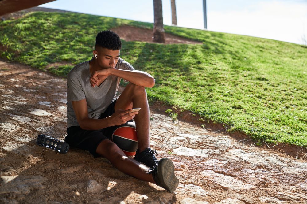 Hispanic sportsman with ball browsing smartphone on street