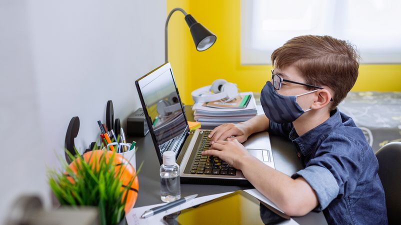 Boy with face mask doing homework with laptop