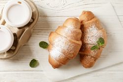 Croissant on wooden table with to go coffee, close up