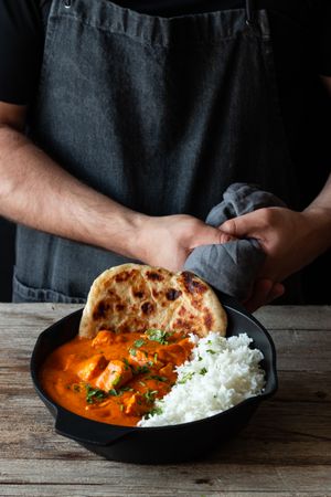 Faceless cook holding frying pan with hot butter chicken