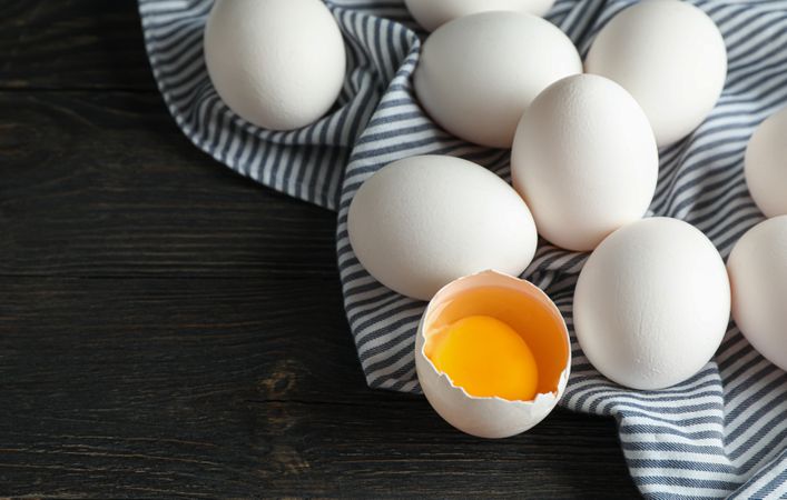chicken eggs in carton box and kitchen towel on wooden table, space for text and closeup