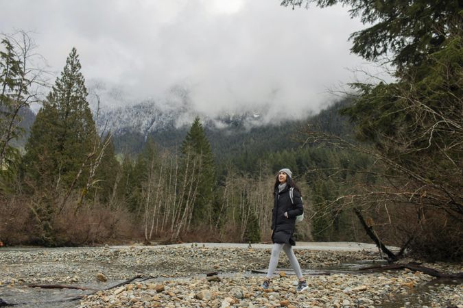 Young female in the mountains standing on river rocks near water