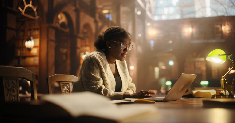 Young Woman Using Laptop for Online Education, Surrounded by Books, Preparing for University Exams.