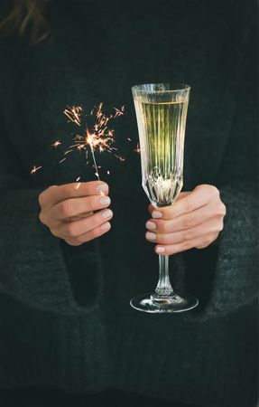 Woman holding crystal flute of champagne and sparkler, grey sweater