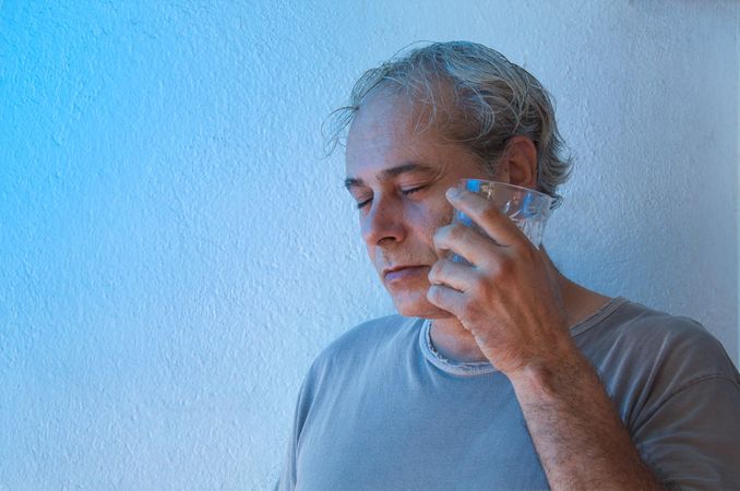 Portrait of middle aged man in gray shirt feeling the coolness of clear glass on his cheek
