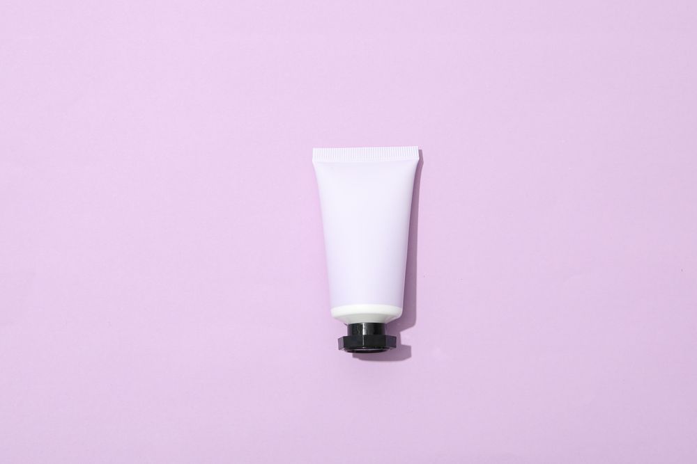 Tube with cream on pink background, top view